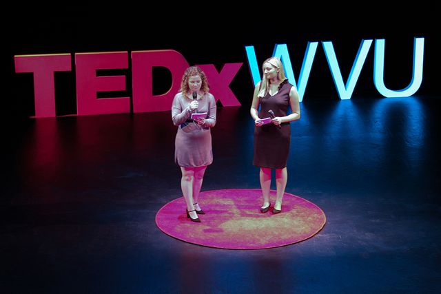 Lauren Moore and Allie Satterfield speaking on stage at the Davis Theatre in front of the large TEDxWVU letters